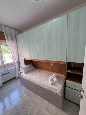 A single bed with a wooden headboard, a bedside table, and a built-in wardrobe with multiple compartments.