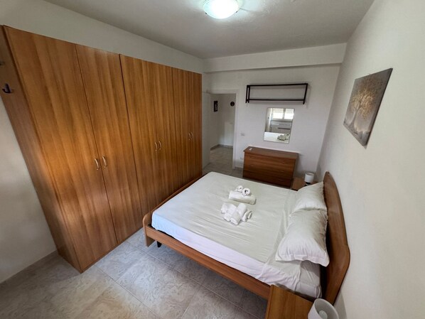 A bedroom with a wooden wardrobe, a bed with white linens, and a small bedside table.
