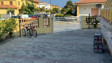 Une allée pavée mène à une entrée fermée par un portail, où sont garés des vélos.