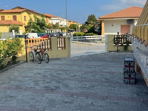 Un camino pavimentado que conduce a una entrada con puerta de acceso, con bicicletas estacionadas.