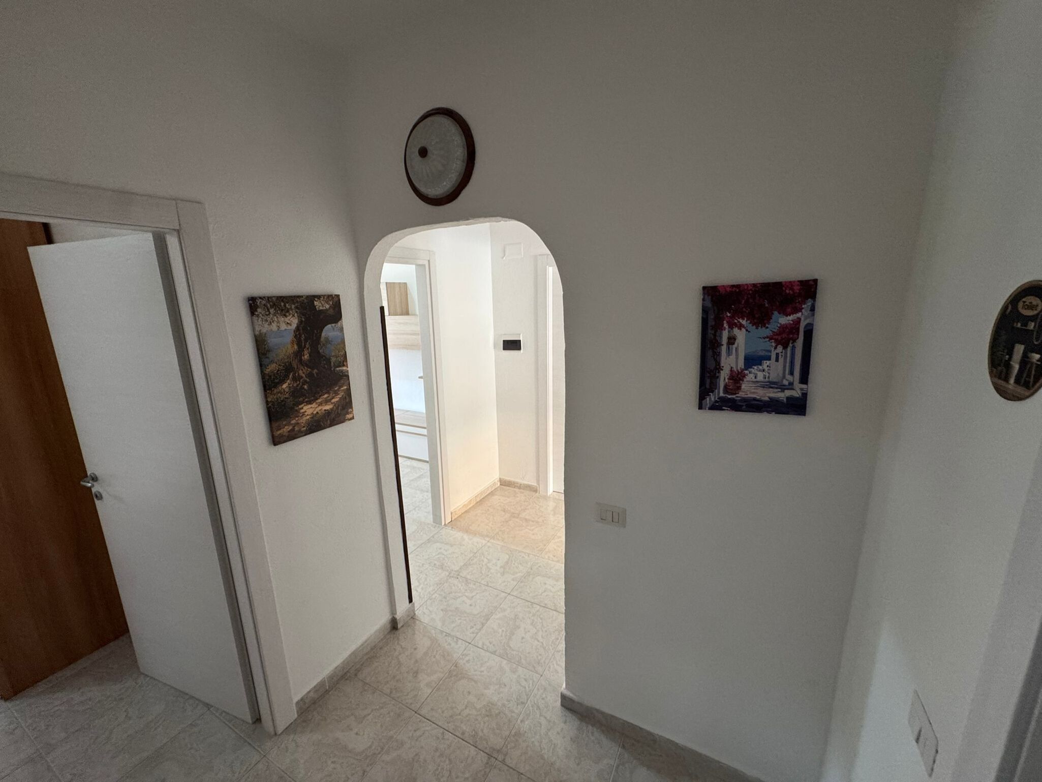A hallway with a door, a painting, a light fixture, and a tiled floor.