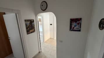 A hallway with a door, a painting, a light fixture, and a tiled floor.