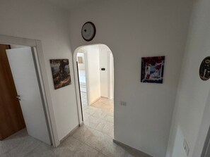 A hallway with a door, a painting, a light fixture, and a tiled floor.