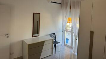 Een kamer met een witte kast, een spiegel, een stoel en een raam met gordijnen.