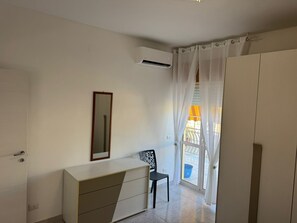 Ein Zimmer mit weißem Kleiderschrank, Spiegel, Stuhl und einem fenster mit Vorhängen.
