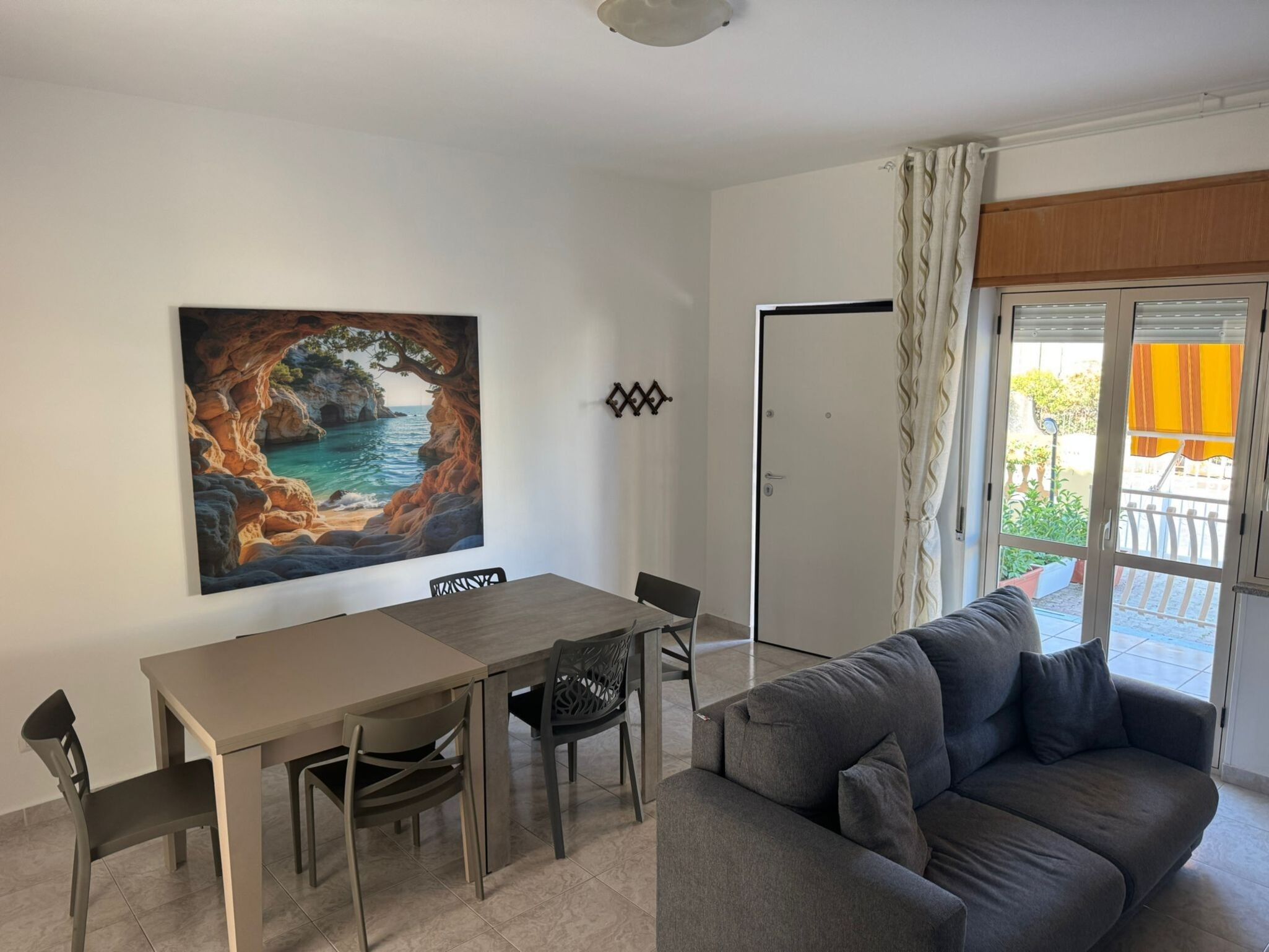 Ein Wohnzimmer mit einer Couch, einem Esstisch mit Stühlen, einem Gemälde einer Küstenlandschaft und einer Glastür zum Außenbereich.