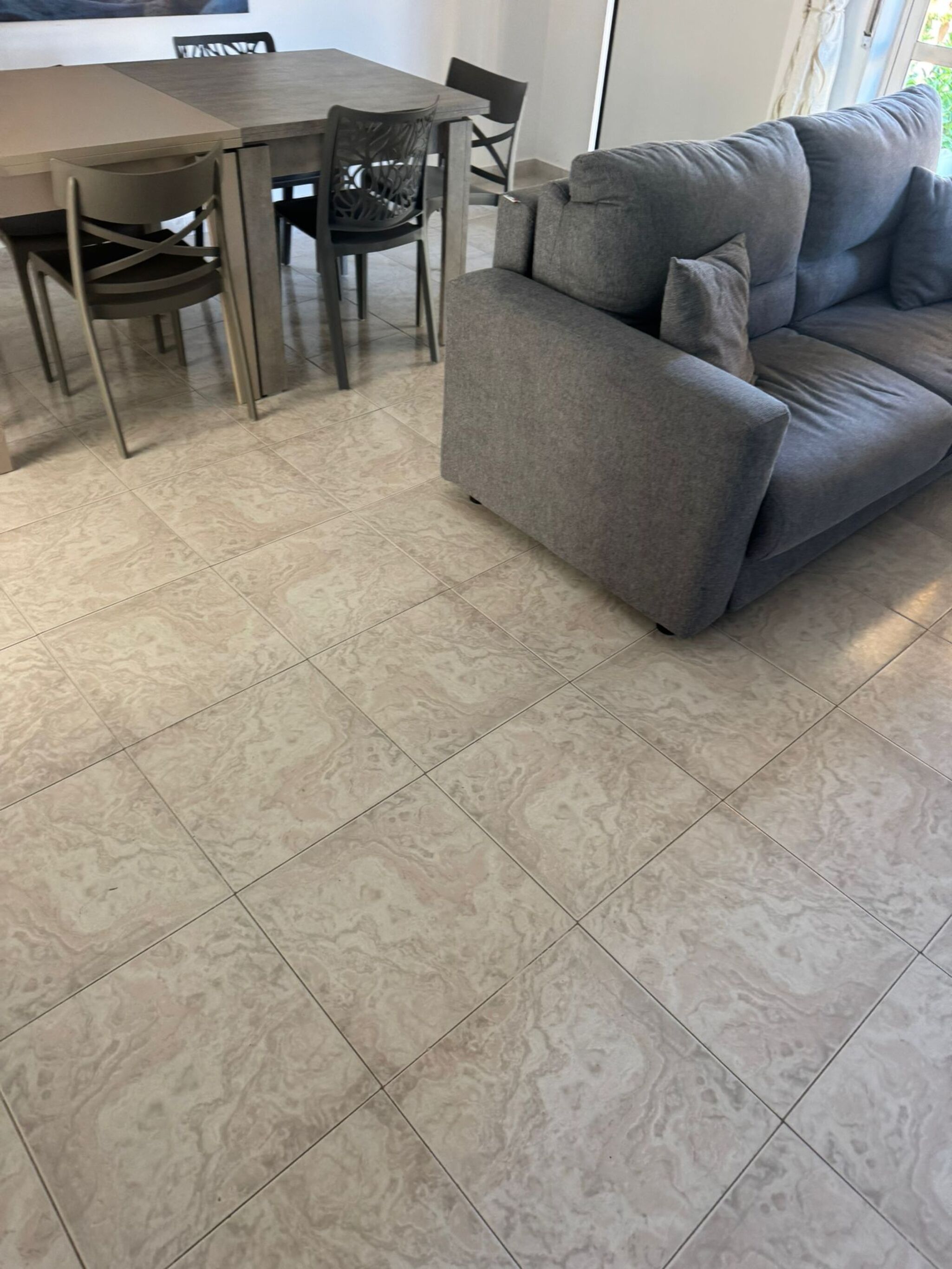 Un salon moderne avec un canapé gris, une table à manger avec des chaises et un sol à motifs.