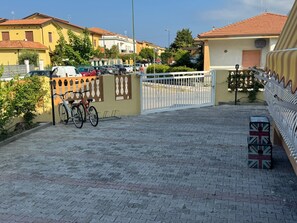 Ein gepflasterter Weg führt zu einem verschlossenen Eingang, wo Fahrräder abgestellt sind.