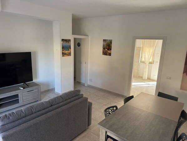 Una sala de estar moderna con televisor de pantalla plana, sofá gris y un comedor con mesa y sillas.