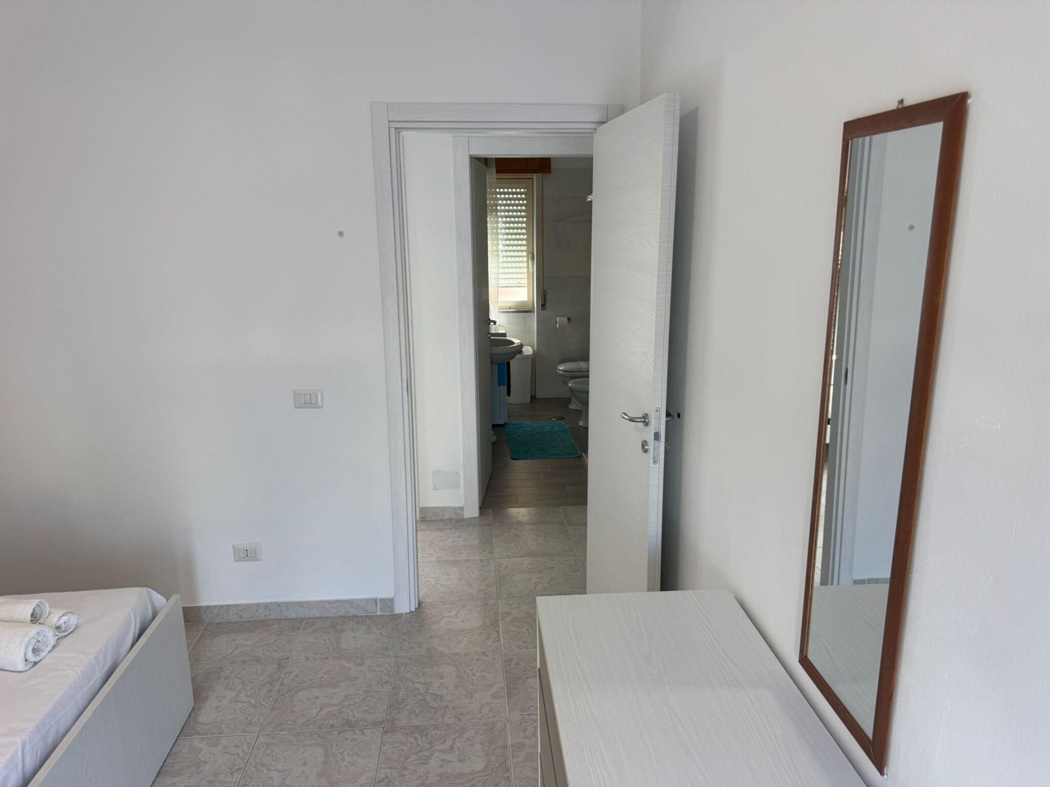 A hotel room with a bed, a bedside table, a mirror, and a bathroom visible through an open door.