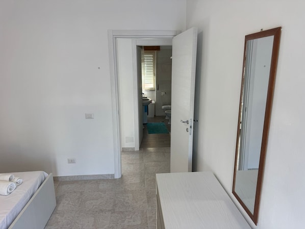 A hotel room with a bed, a bedside table, a mirror, and a bathroom visible through an open door.