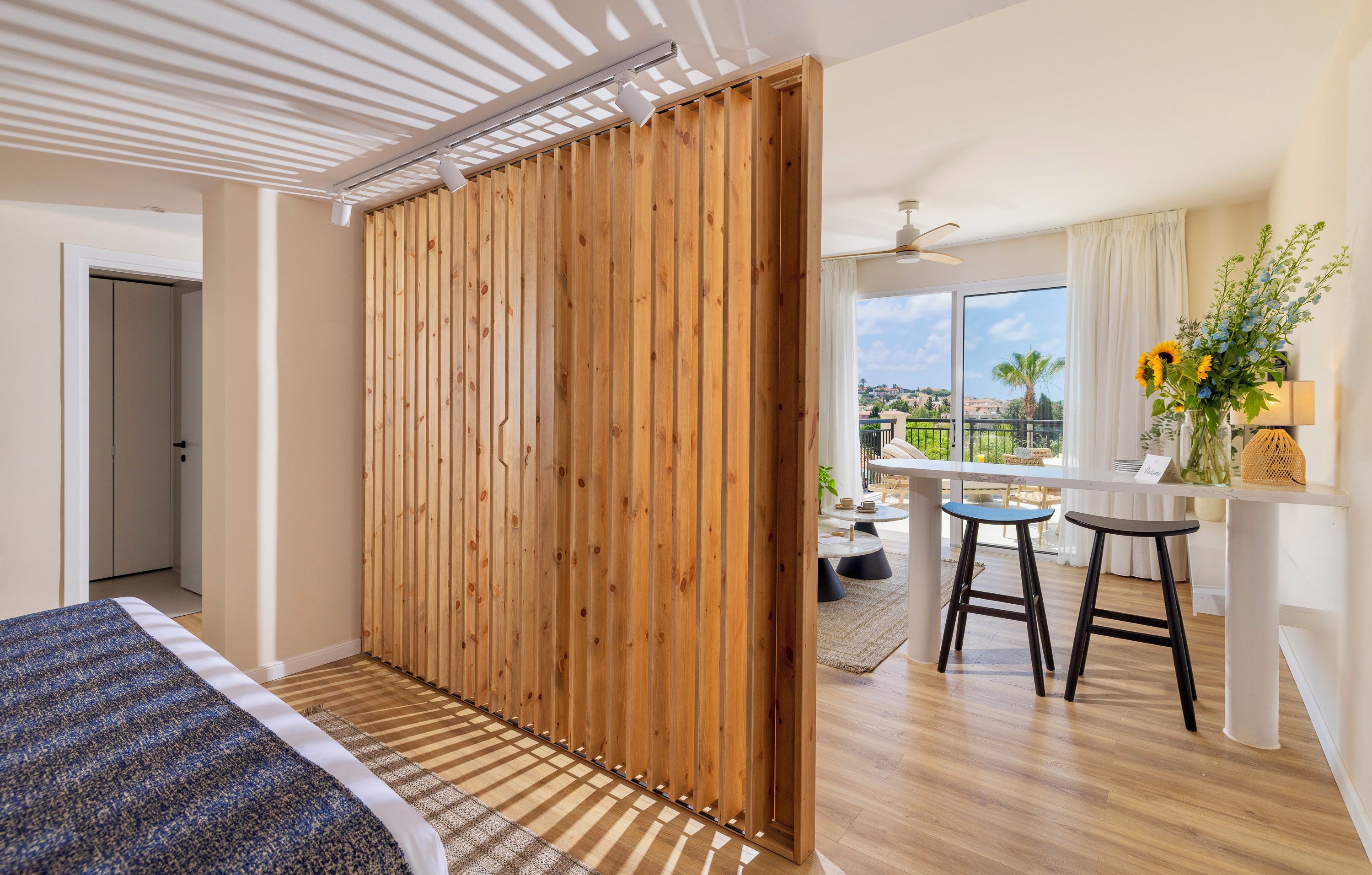 Ein Schlafzimmer mit Bett, einer Holzwand und Blick auf einen Balkon mit Tisch und Stühlen.