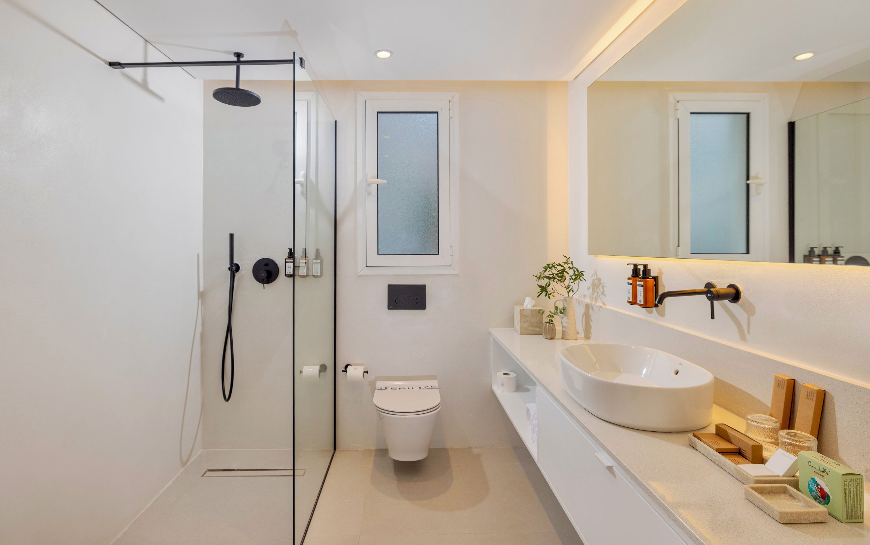 Une salle de bain moderne avec une douche à parois de verre, des toilettes, un grand lavabo et un miroir au-dessus du lavabo.