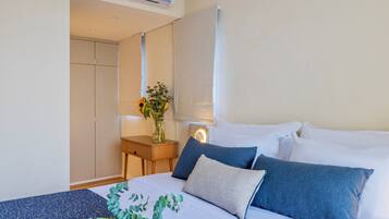 A bedroom with a bed, pillows, a nightstand, a vase with flowers, and a wardrobe.