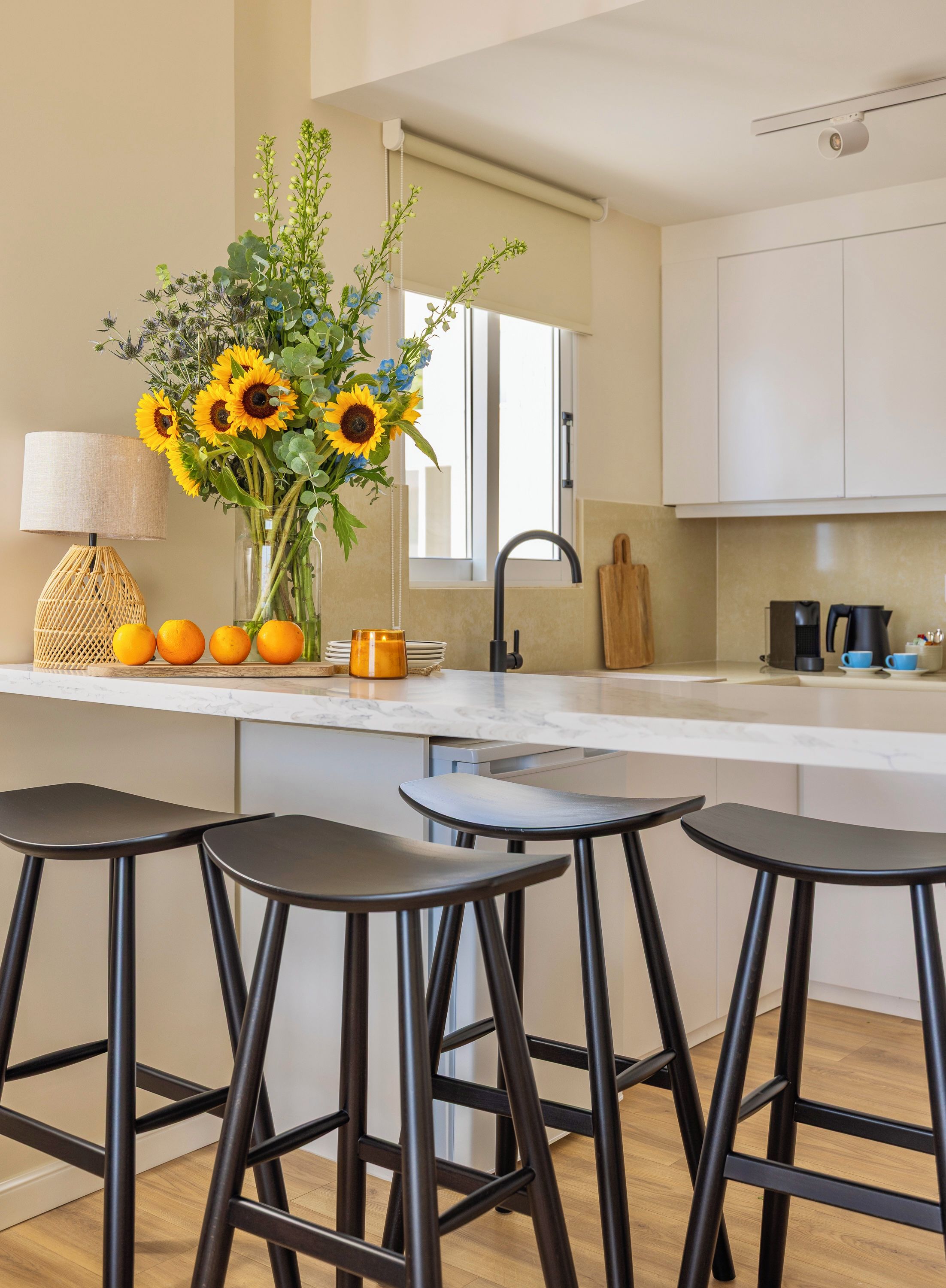 Eine moderne Küche mit Marmorarbeitsplatte, einer Vase mit Sonnenblumen und drei schwarzen Barhocker.