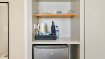 Cocina compacta con refrigerador incorporado, cafetera y repisa con tetera y tazas.