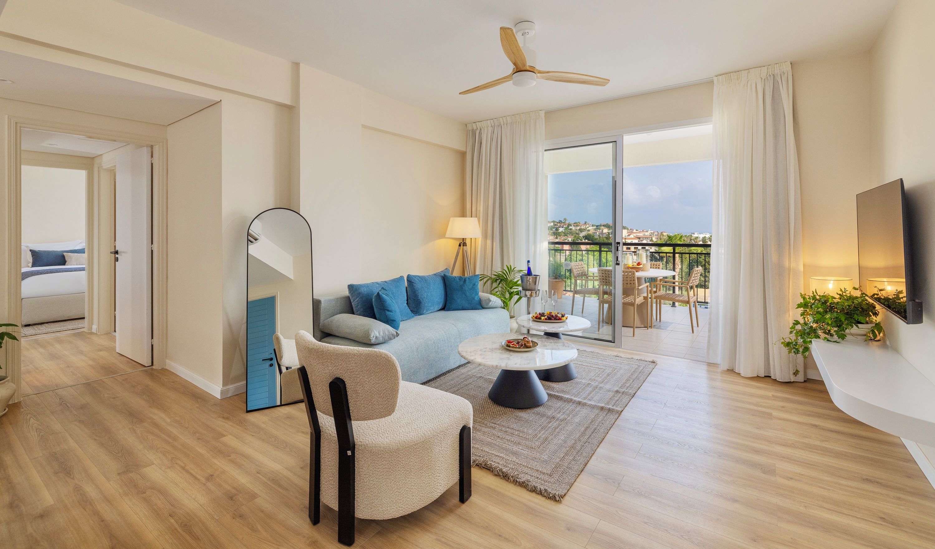 A modern living room with a sofa, armchair, coffee table, and a balcony with a table and chairs.