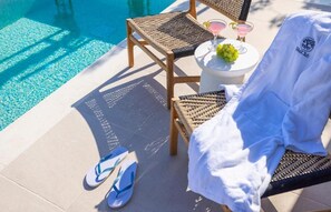 A poolside area with a lounge chair, a small round table with drinks, and a pair of flip-flops on the ground. - LiBa (Chlorakas)