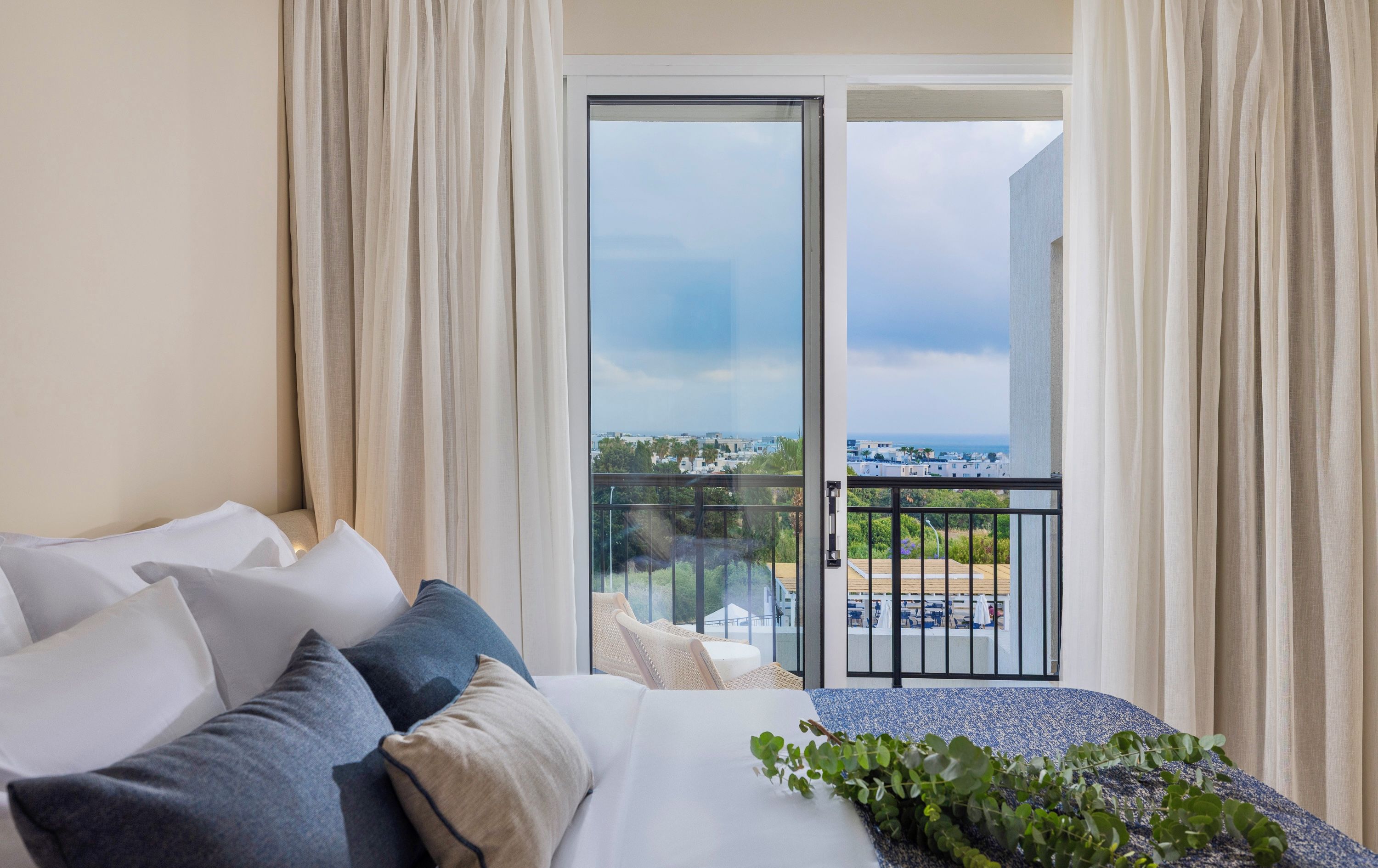A hotel room with a bed, a balcony with a view of the city, and a dining area with outdoor seating.