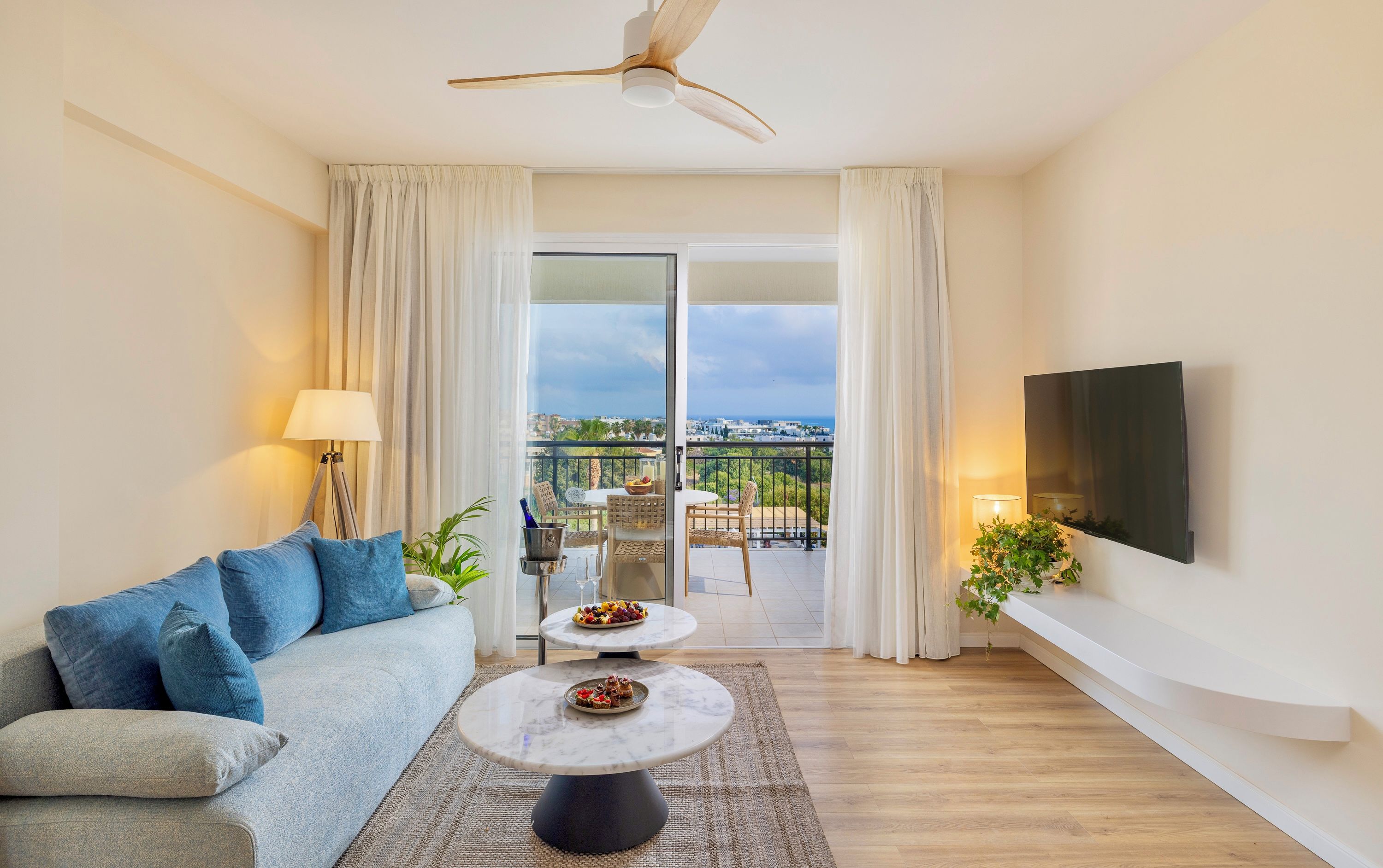 A modern living room with a sofa, a coffee table, a TV, and a balcony with a view.