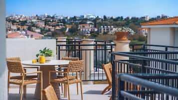 Una terraza con sillas de mimbre y una mesa, una planta en maceta y vistas a un paisaje urbano.