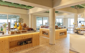 Un amplio vestíbulo de hotel con mostradores de recepción de madera, diversas plantas y vistas al exterior a través de grandes ventanales.
