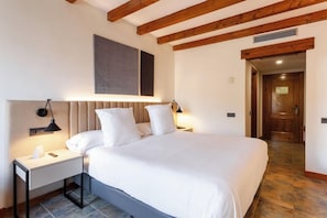 Habitación de hotel con una cama grande, mesitas de noche, cabecera con iluminación integrada y techo de madera, además de una puerta que da a otra habitación.