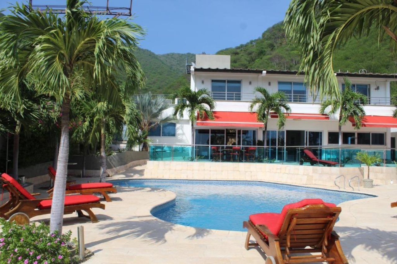 Ein Poolbereich mit Liegestühlen, ein Gebäude mit rotem Markisenvorzelt und ein Berg im Hintergrund.