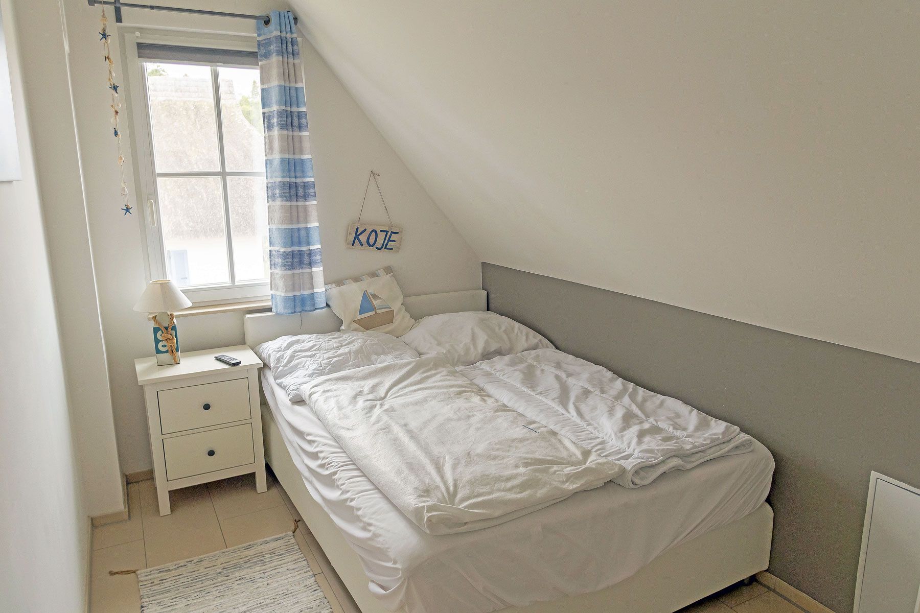 Ein Schlafzimmer mit einem Einzelbett, einem Nachttisch, einer Lampe und einem Fenster mit Vorhängen.