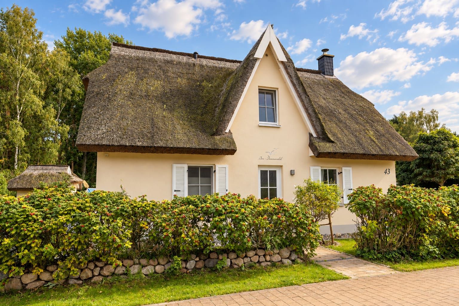 A traditional house with a steeply pitched roof, a stone wall, and a well-maintained garden.