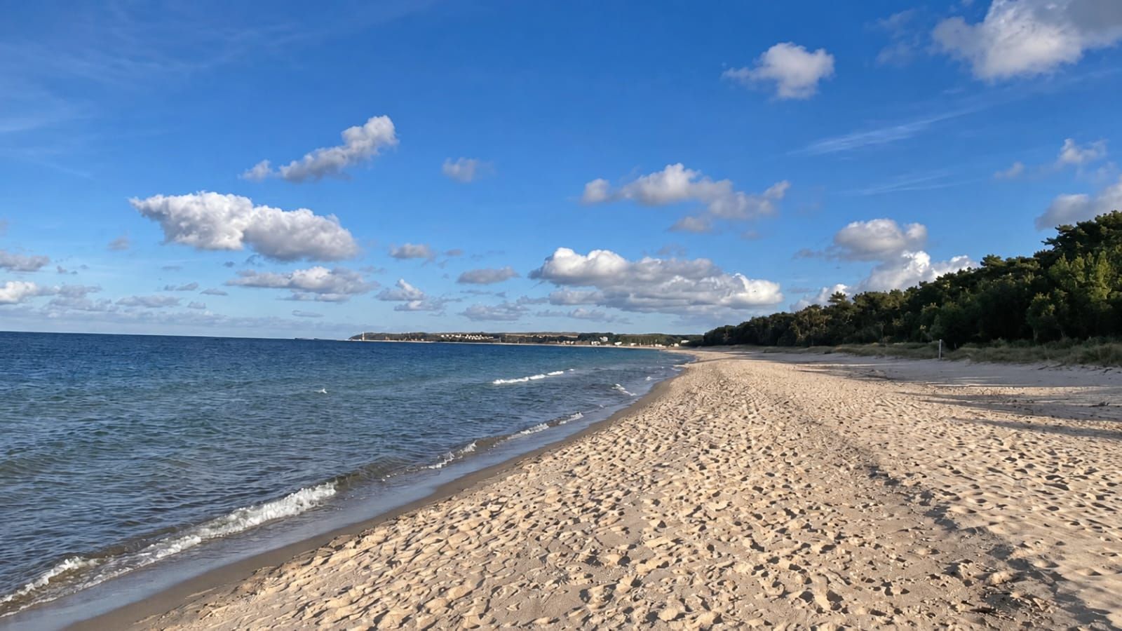 A sandy beach with gentle waves, a clear sky, and a distant shoreline.