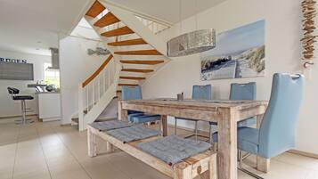 Ein Essbereich mit Holztisch und blauen Stühlen, eine Treppe mit Holzstufen und im Hintergrund ein Küchenbereich.