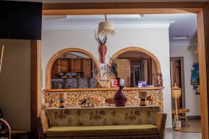 Un salón con sofá, una mesita de centro y una pared de madera con diseño de troncos. Se ve una cocina a través de un arco.
