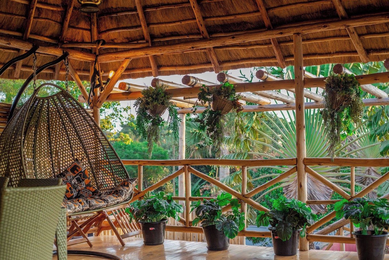 Una estructura de madera con techo de paja, plantas colgantes y una silla tejida.