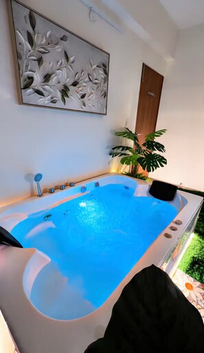 A spa area with a hot tub, a wall-mounted artwork, a wooden door, and a potted plant. - RapidNest Jakkur A Luxury Stay with Jacuzzi (Bangalore)