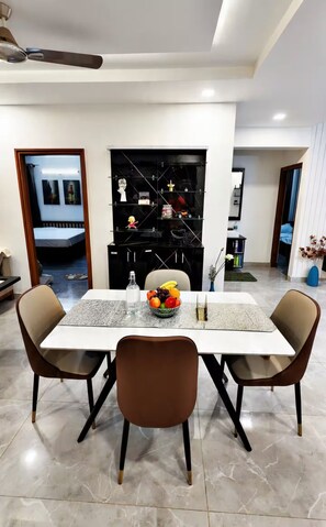A dining area with a table set for two, chairs, a fruit bowl, and a black shelving unit with various items. - RapidNest Jakkur A Luxury Stay with Jacuzzi (Bangalore)