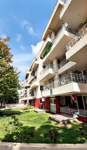 A multi-story residential building with balconies, a lawn, and a clear sky. - RapidNest Jakkur A Luxury Stay with Jacuzzi (Bangalore)