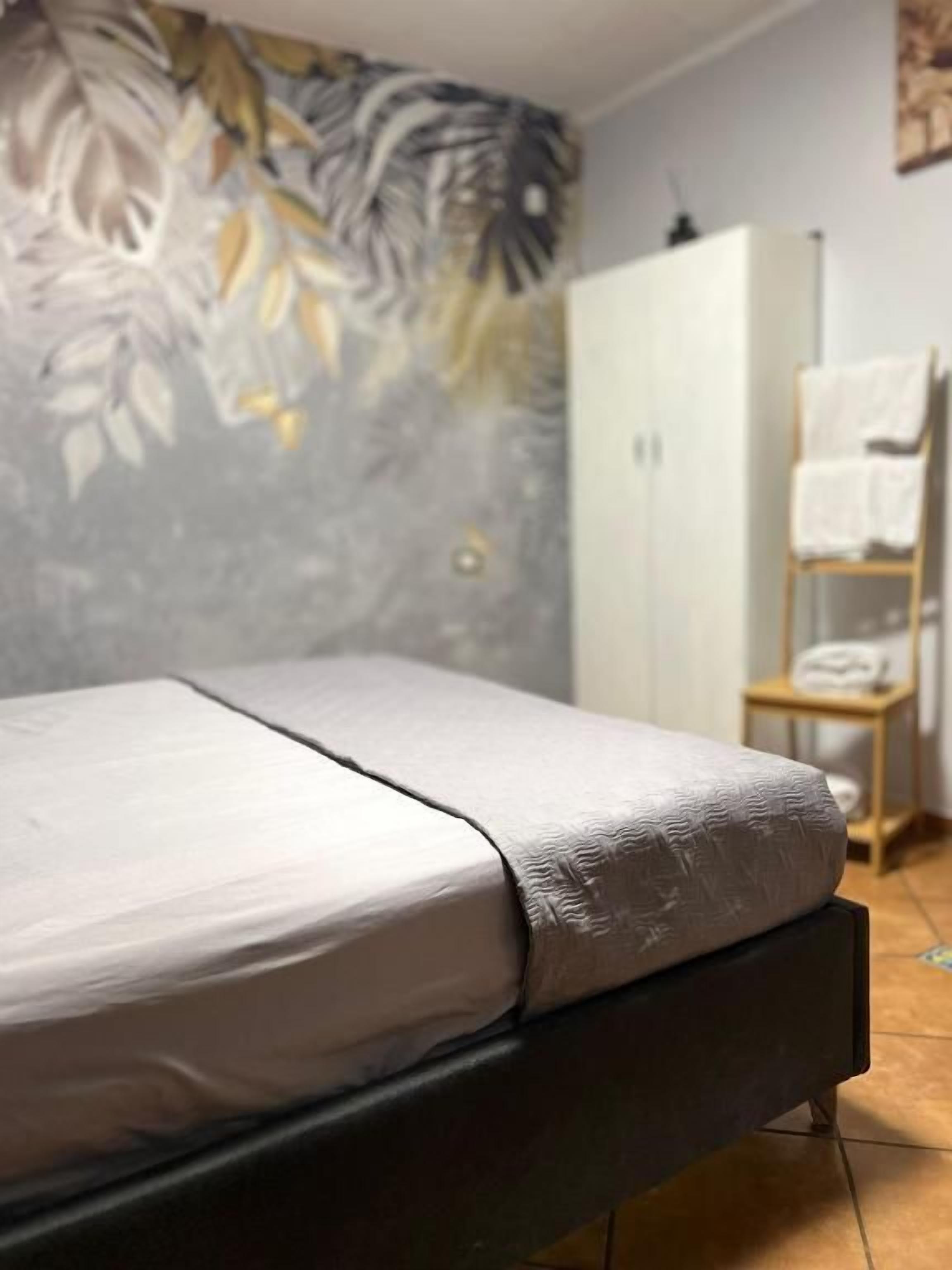 Una cama con colchón blanco y estructura oscura, un armario y una estantería con toallas.
