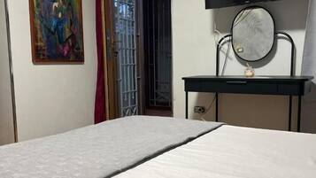 Een slaapkamer met een bed, een aan de muur bevestigde televisie en een deur die naar een andere kamer leidt.