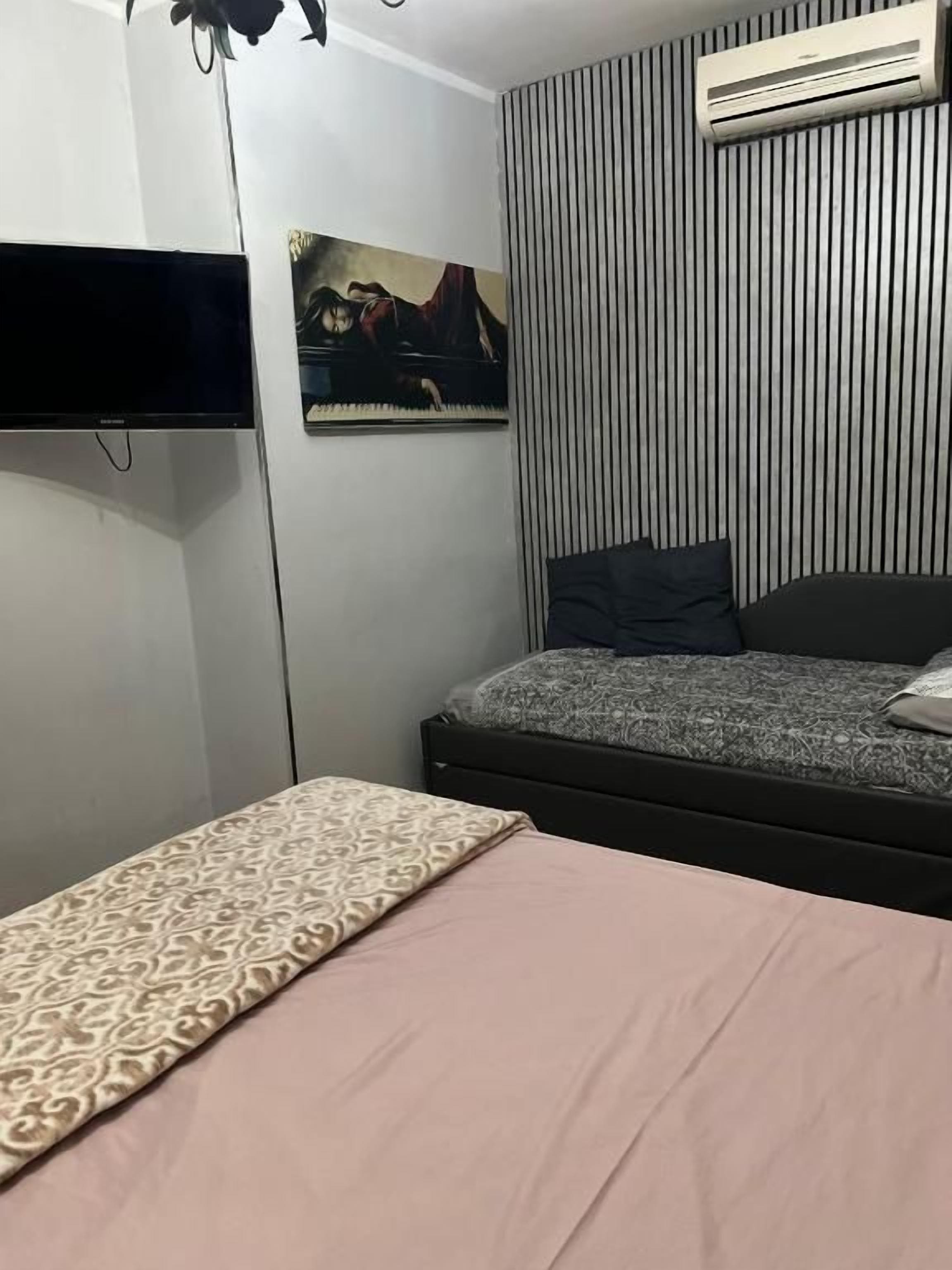 A bedroom with a bed, a flat-screen TV mounted on the wall, a painting, and a striped wall.