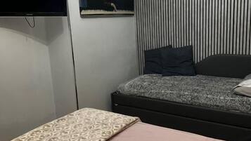 A bedroom with a bed, a flat-screen TV mounted on the wall, a painting, and a striped wall.