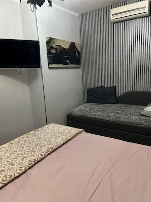 Un dormitorio con cama, un televisor de pantalla plana en la pared, un cuadro y pared a rayas.