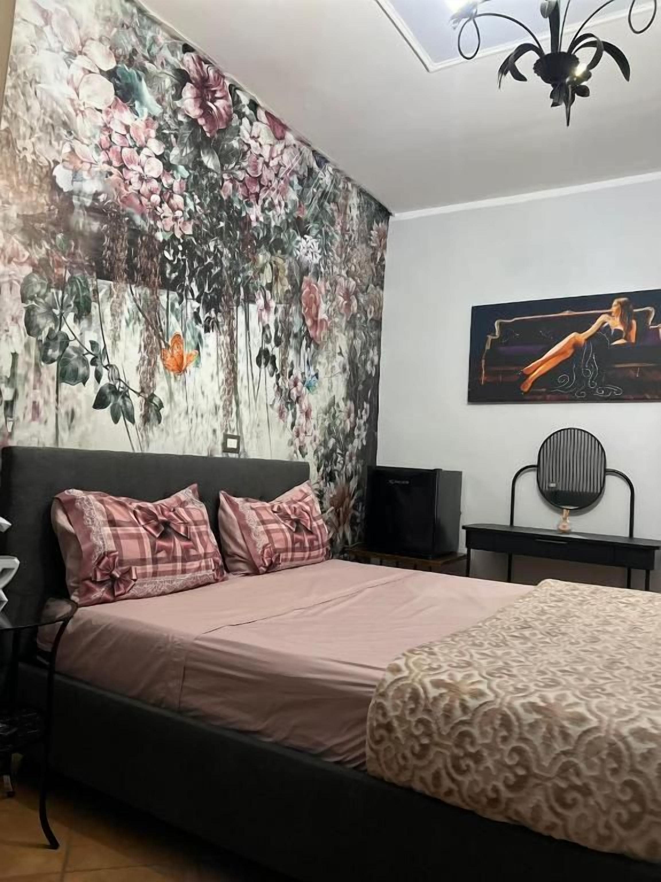 Quarto com cama, televisão na parede, uma cadeira e luminária no teto.