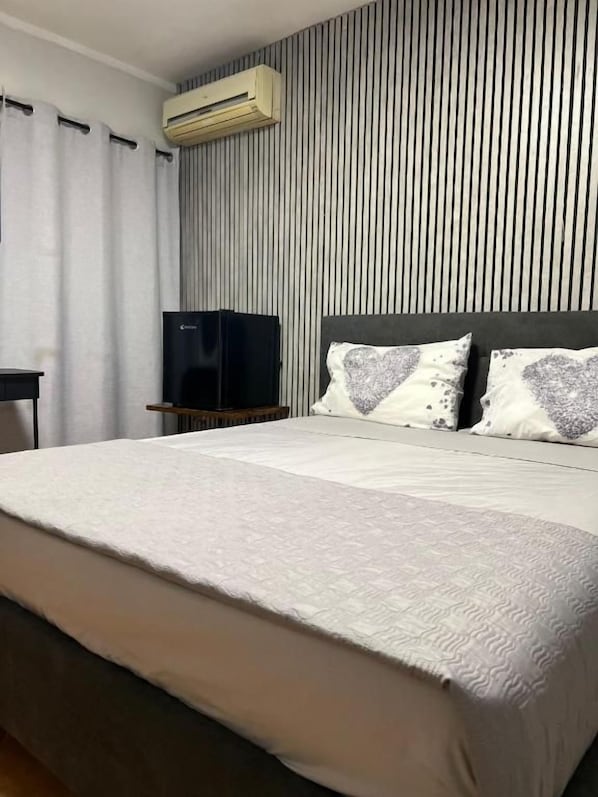 Habitación de hotel con una cama grande, un televisor de pantalla plana y un aire acondicionado instalado en la pared.