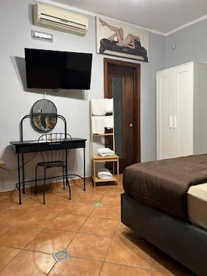 A bedroom with a bed, a desk with a chair, a television, a wardrobe, and a door.
