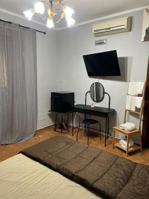 Un dormitorio con cama, escritorio con computadora, silla, televisor y unidad de aire acondicionado.