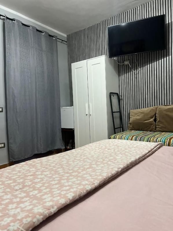 Un dormitorio con cama, televisor montado en la pared, armario y cortina.