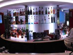 A bar area with multiple shelves of liquor bottles, a counter with bar tools, and a television screen. - Sigona Golf Club (Kikuyu)