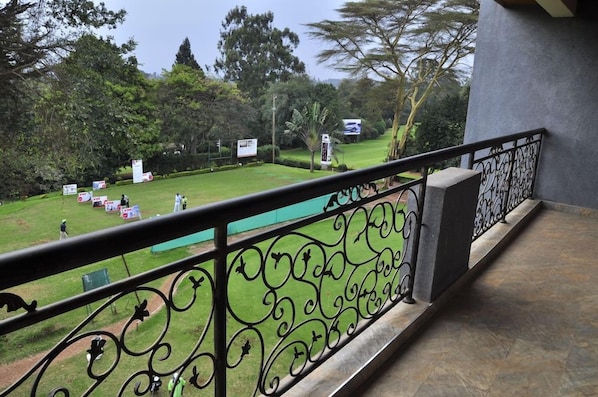 A balcony with a wrought iron railing overlooking a grassy area with trees and a building in the background. - Sigona Golf Club (Kikuyu)