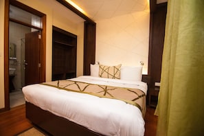Une chambre d’hôtel avec un grand lit, un dressing et une salle de bain visible à travers une porte ouverte.